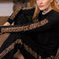 A woman with red hair sits on a brown couch wearing a black long-sleeve pajama set with leopard print stripes on the sleeves and legs.