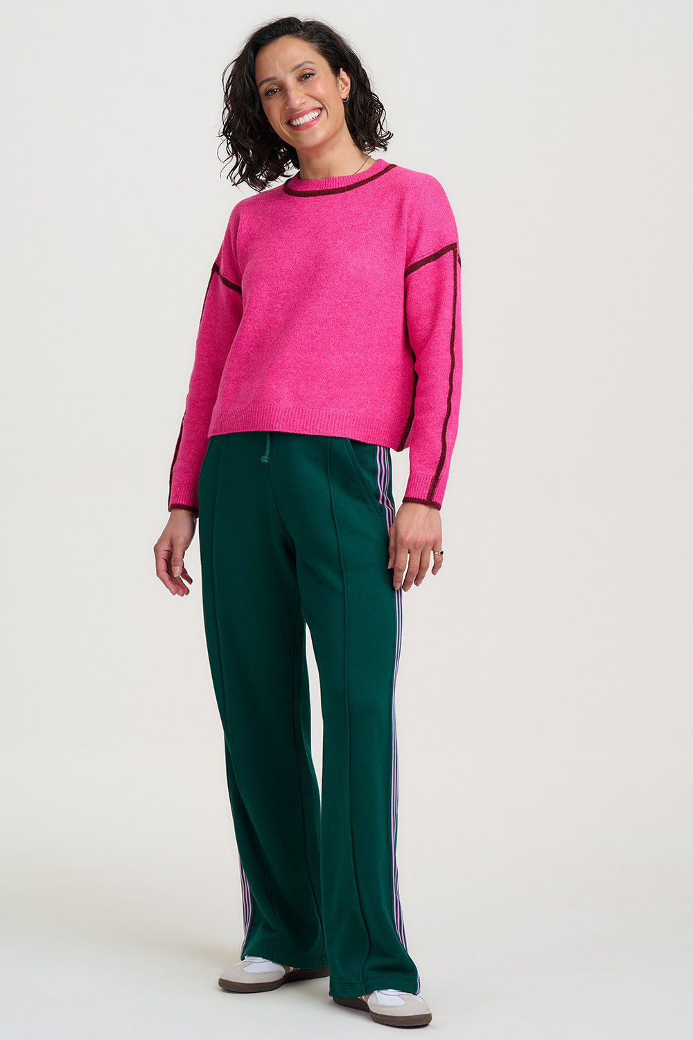 Woman wearing a pink sweater with black trim and green pants on a white background