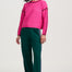 Woman wearing a pink sweater with black trim and green pants on a white background