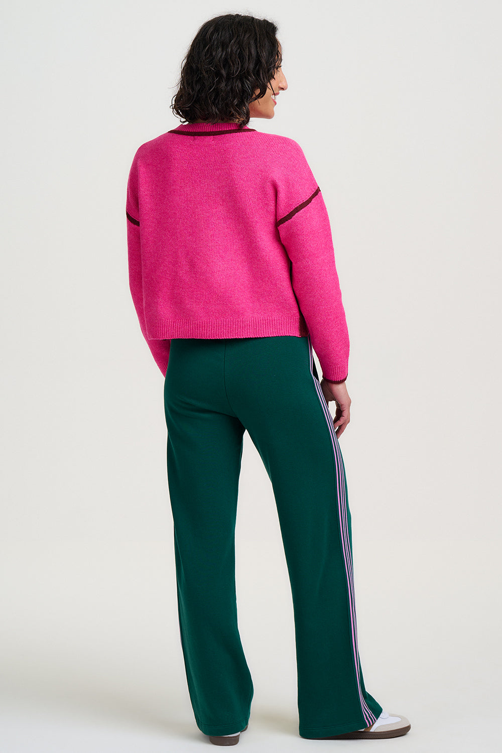Person wearing a pink sweater and green pants with white sole shoes on a white background