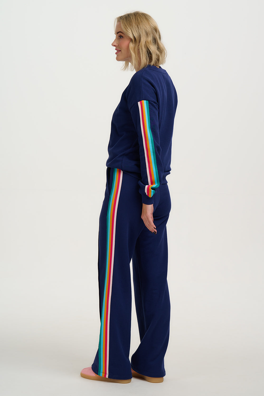 Woman wearing a navy tracksuit with rainbow stripes on a white background