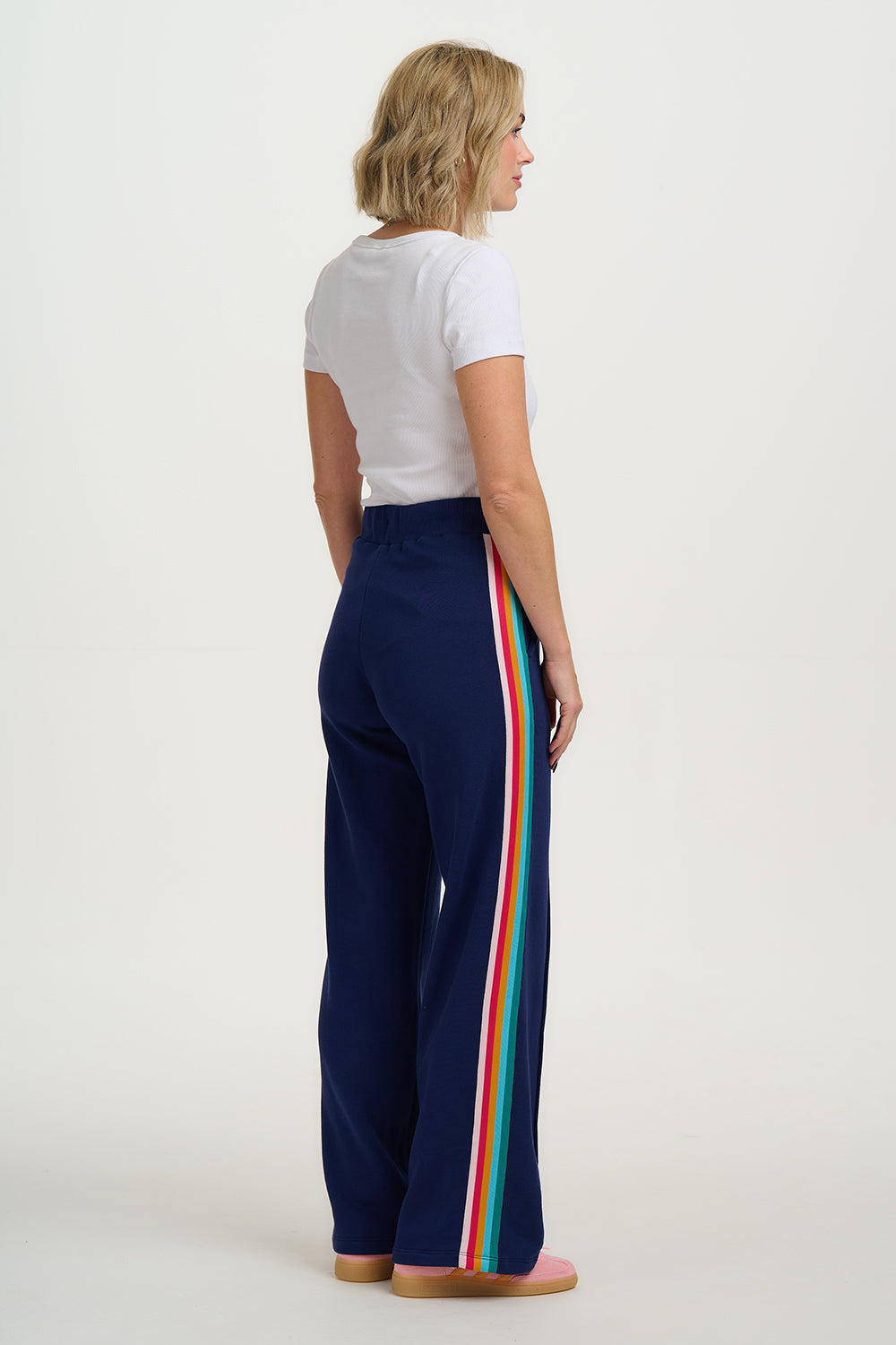 Woman wearing navy pants with rainbow stripes on a white background