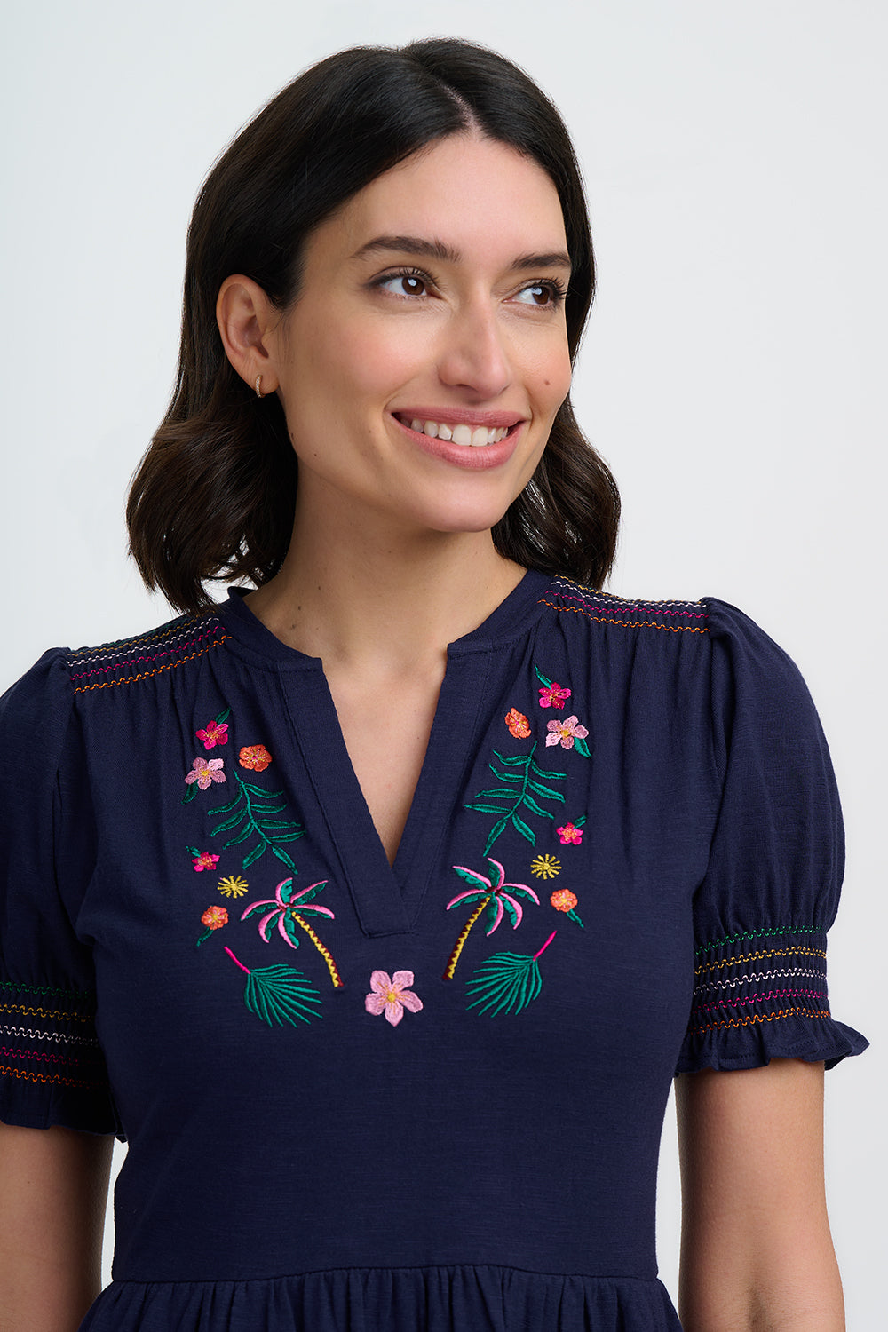 Woman wearing a navy blue dress with colorful embroidery on a white background