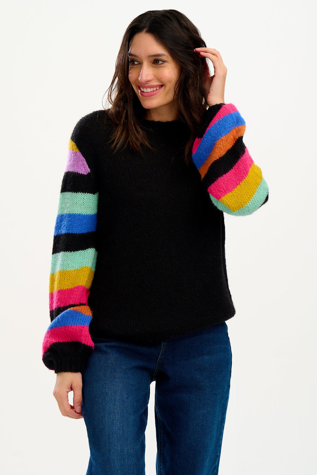 A woman wearing a black sweater with ribbed cuffs and vibrant rainbow-colored sleeves, paired with blue jeans.