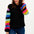 A woman wearing a black sweater with ribbed cuffs and vibrant rainbow-colored sleeves, paired with blue jeans.