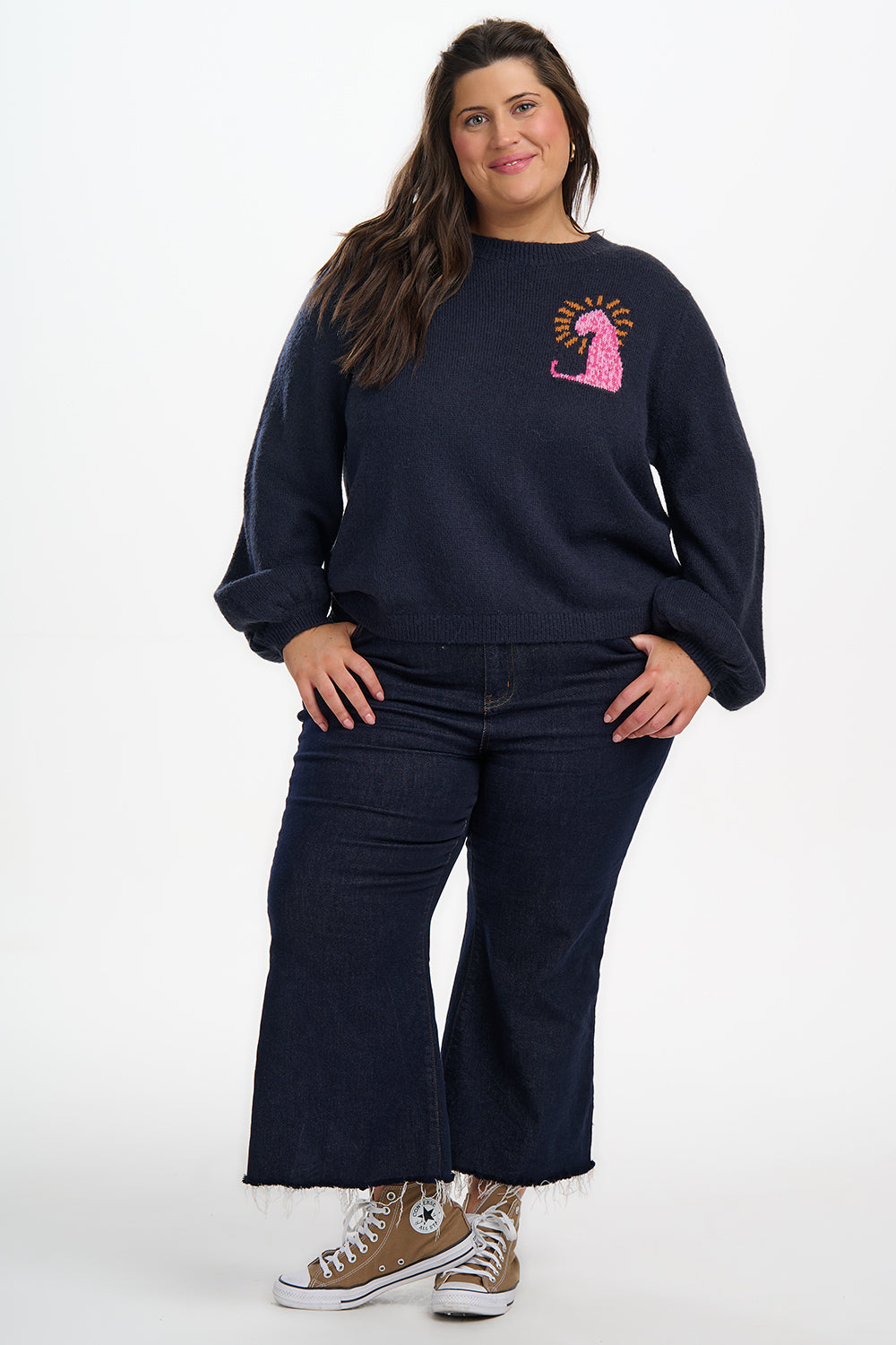 Woman wearing a navy sweatshirt with a pink graphic and dark jeans on a white background