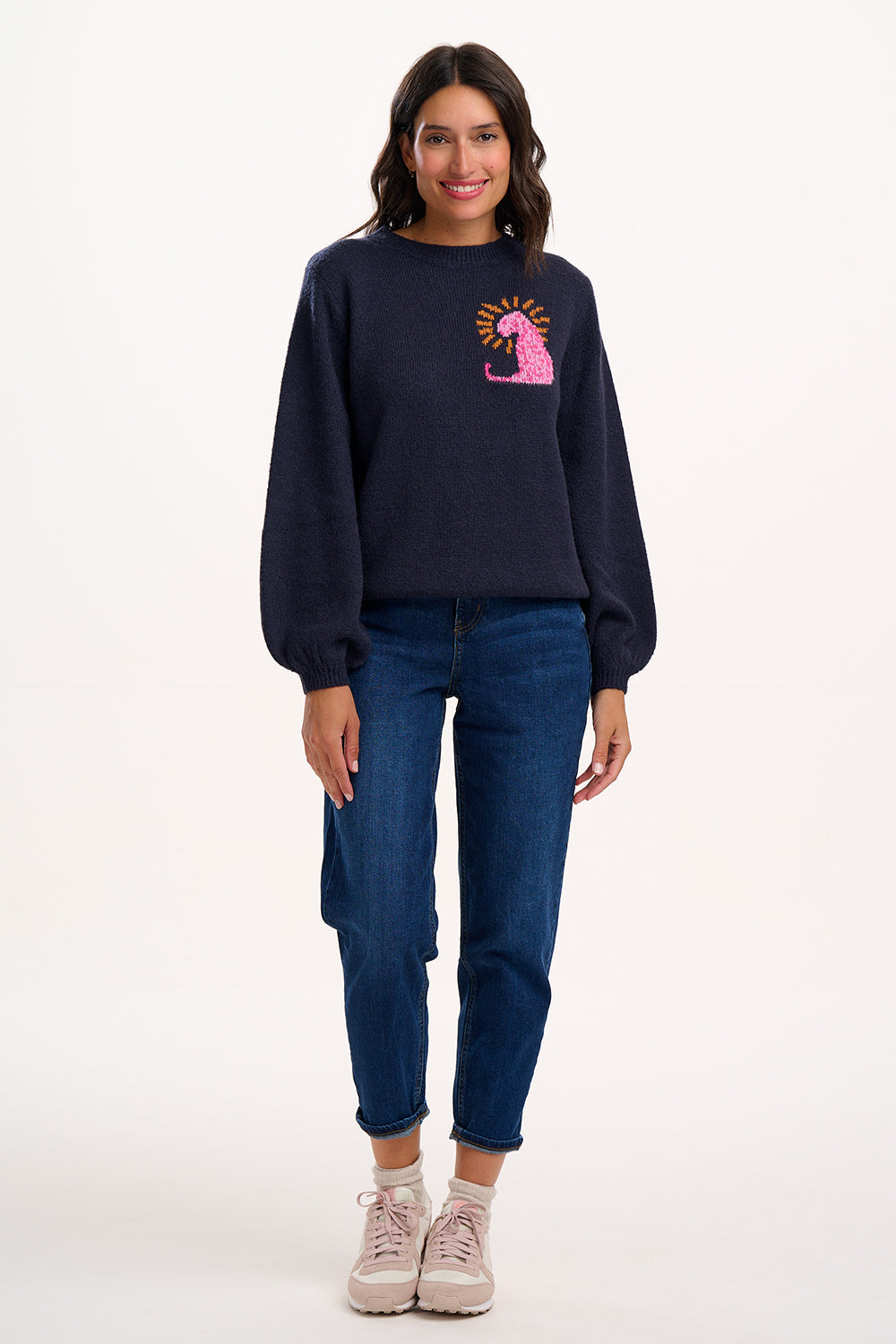 Woman wearing a navy sweatshirt with a pink graphic and blue jeans on a white background