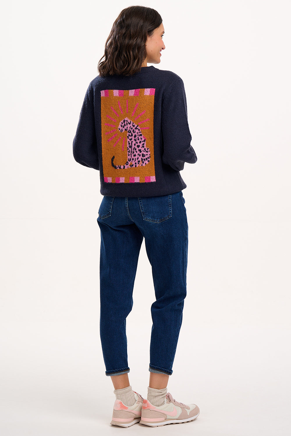 Person wearing a navy blue sweatshirt with a colorful leopard design on the back, standing against a white background.