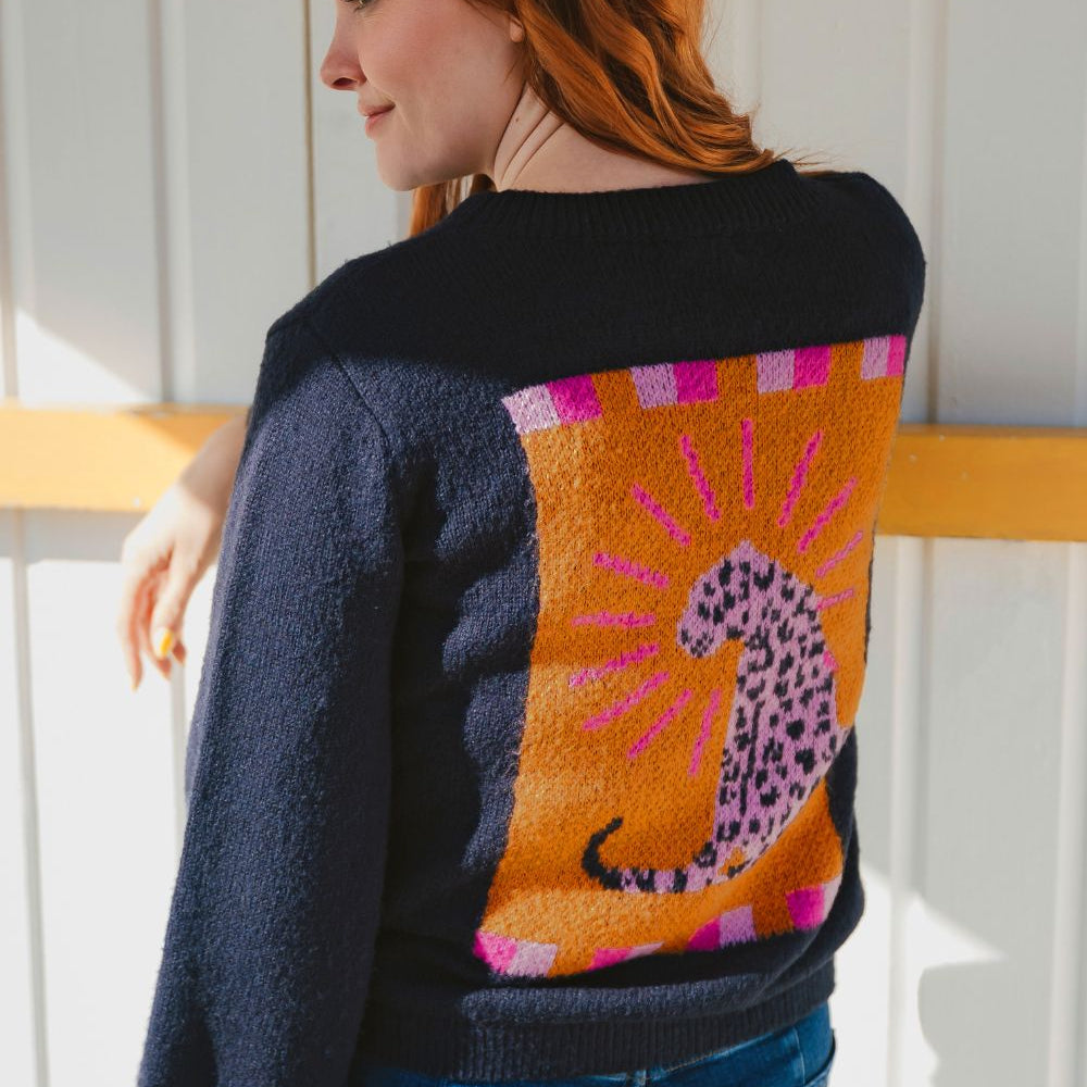 Person wearing a black sweater with a colorful abstract design, standing against a white wall.
