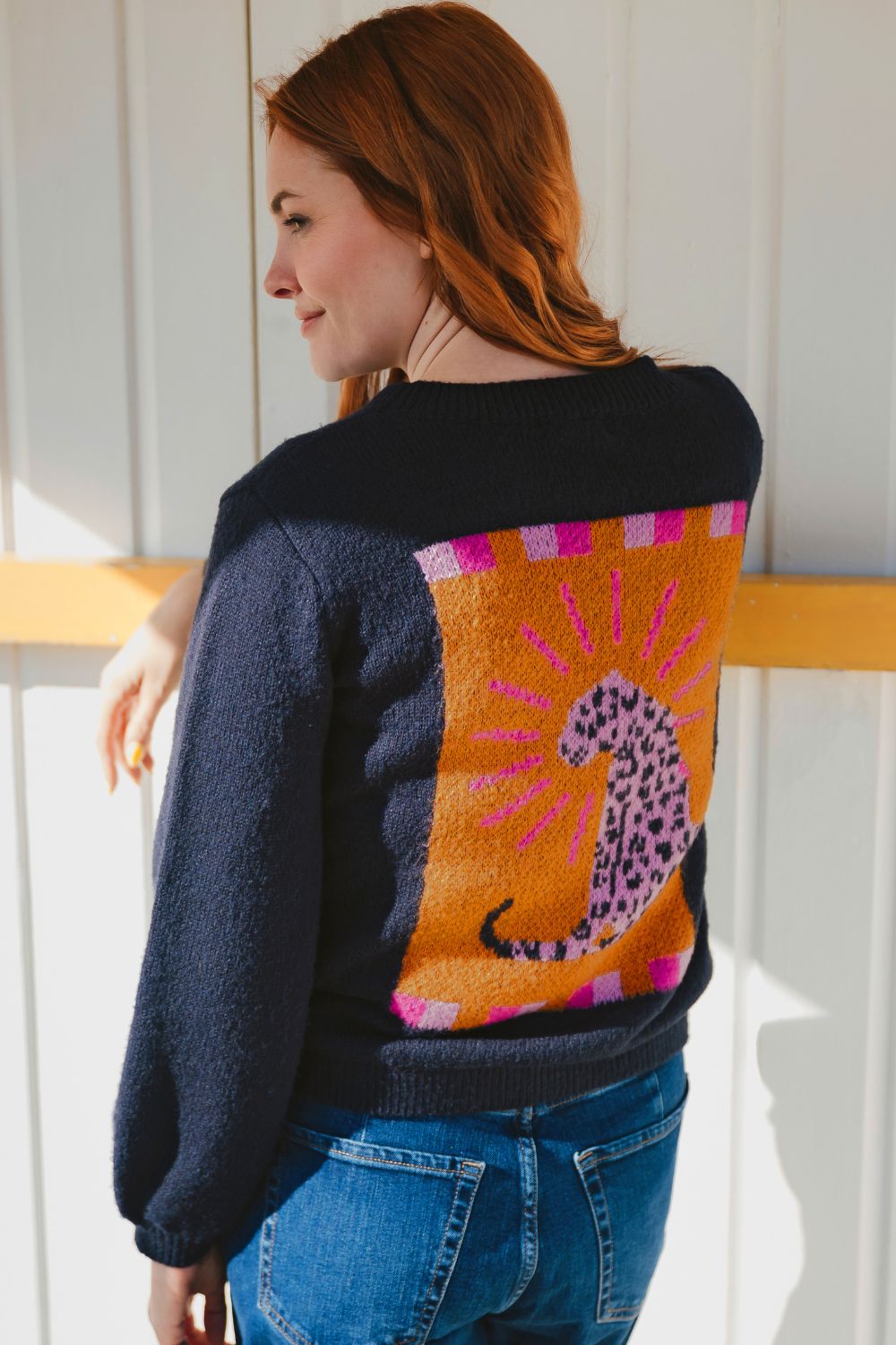Person wearing a black sweater with a colorful abstract design, standing against a white wall.