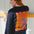 Person wearing a black sweater with a colorful abstract design, standing against a white wall.