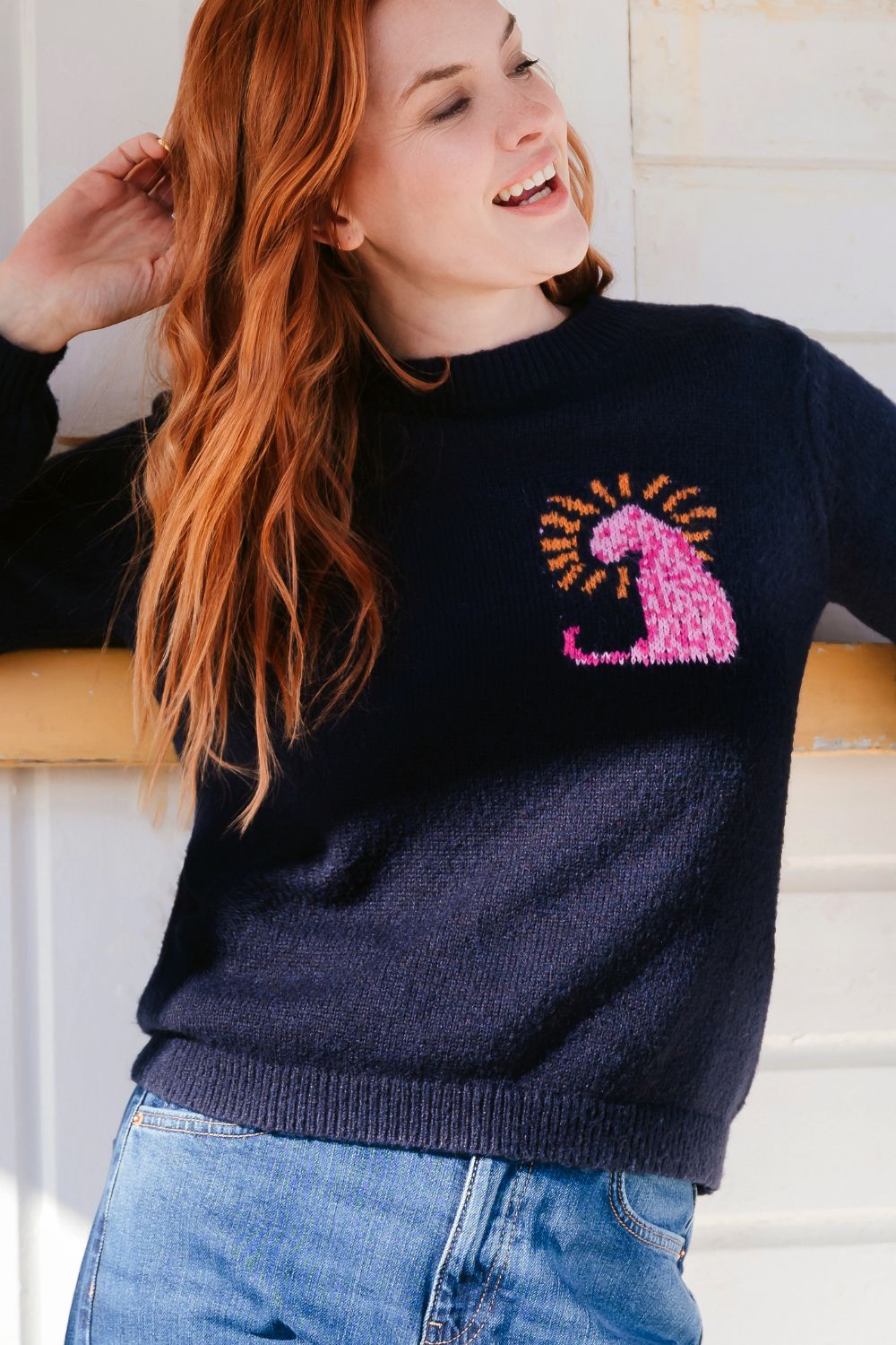 Person wearing a navy sweater with a pink and yellow design, standing against a light-colored wall.