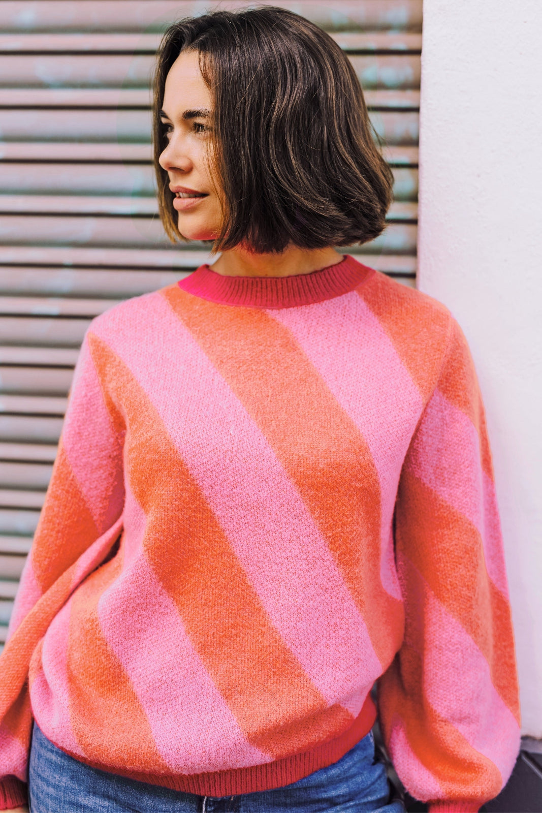 A woman wearing a pink and orange diagonal striped jumper with a round neckline and long sleeves.