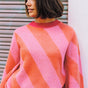 A woman wearing a pink and orange diagonal striped jumper with a round neckline and long sleeves.