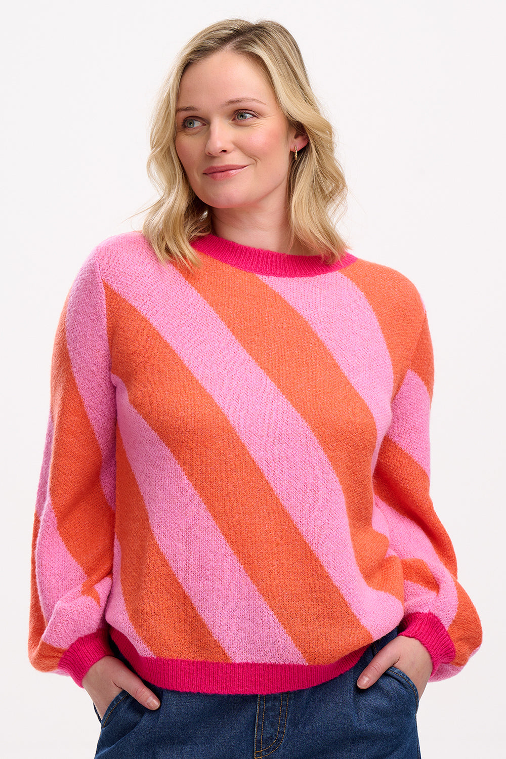 A woman wearing a pink and orange diagonal striped jumper with a round neckline and long sleeves.