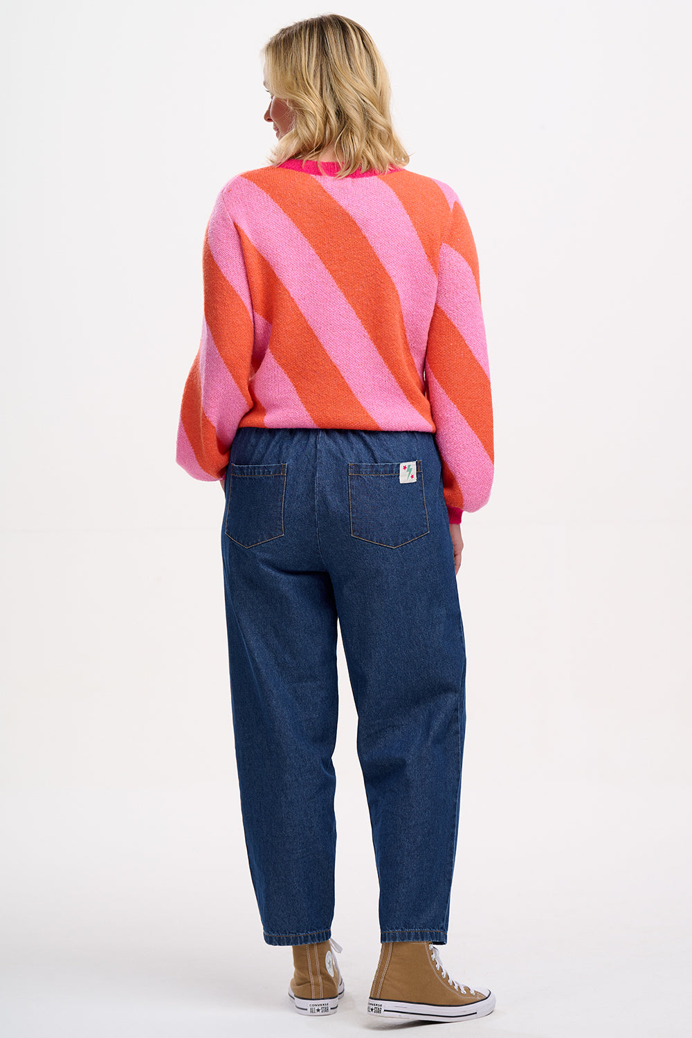 A woman wearing a pink and orange diagonal striped jumper with a round neckline and long sleeves.