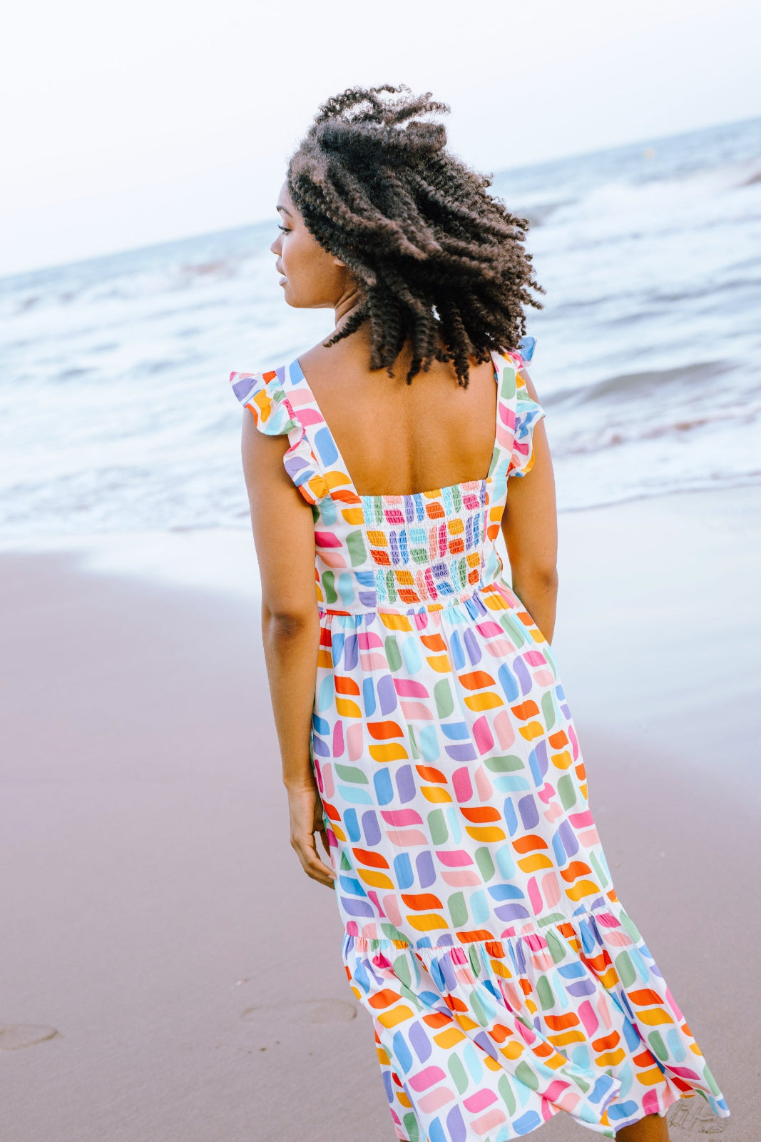 A model wearing an off-white midi sundress with a curved geometric print, featuring a shirred back panel and tiered skirt.