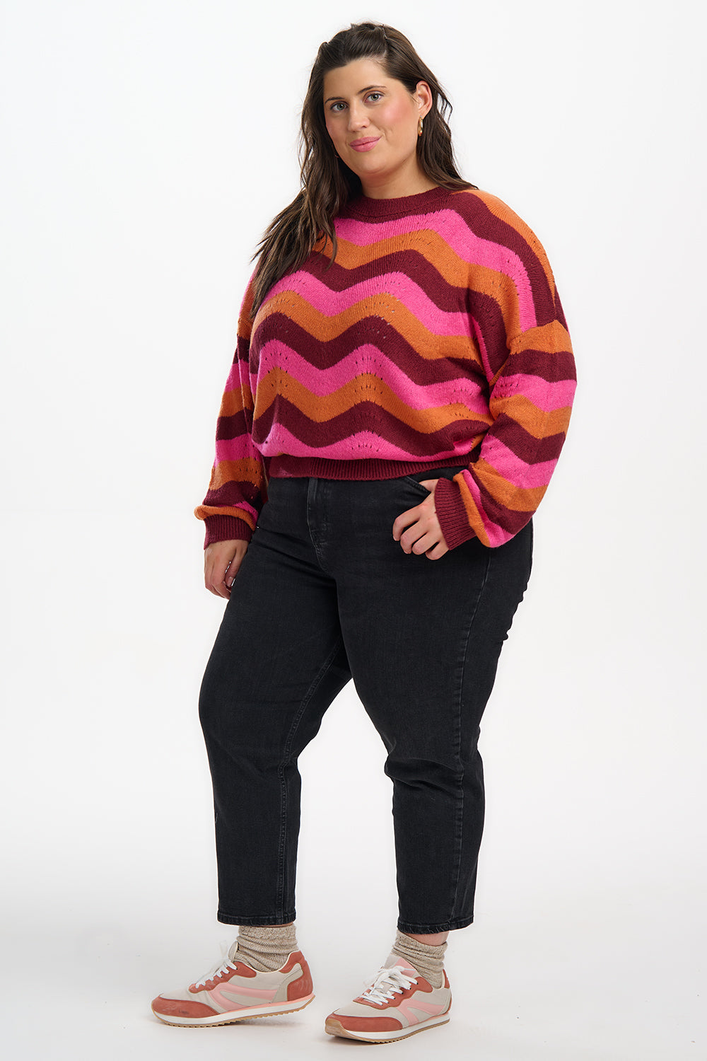 Woman wearing a colorful striped sweater and black jeans on a white background