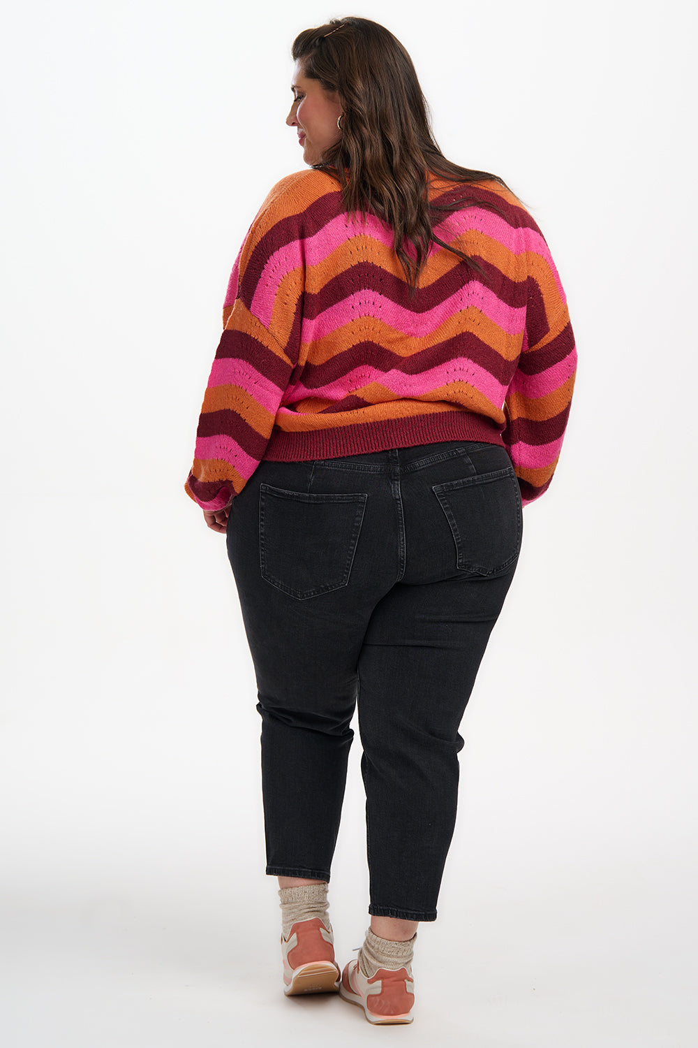 Person wearing a colorful striped sweater and black pants on a white background
