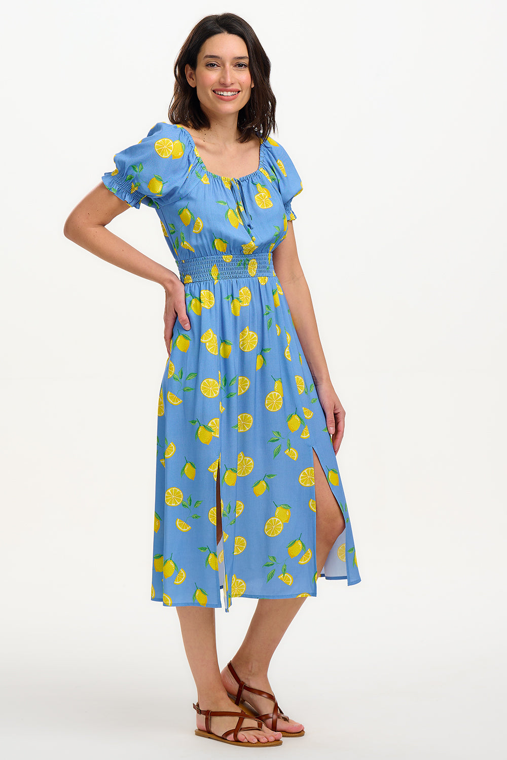 A woman modeling a midi dress with an off-the-shoulder neckline, featuring a blue color with yellow lemon print. The dress has frill-cuffed short sleeves and two front splits in the skirt.