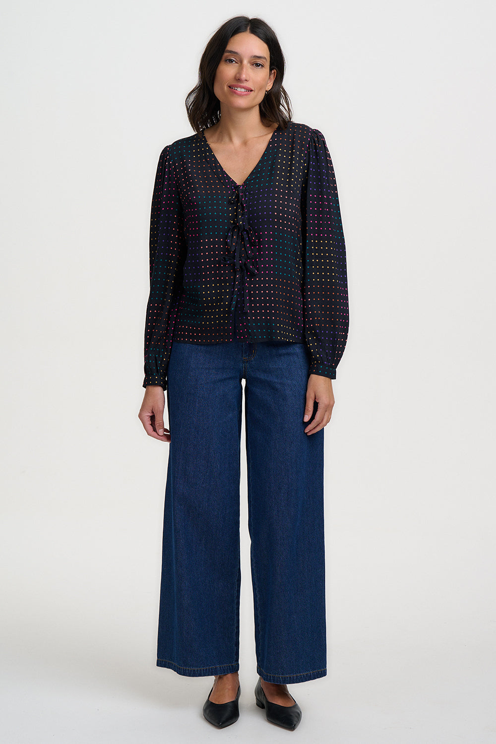 Woman wearing a dark patterned blouse and wide-leg jeans on a white background