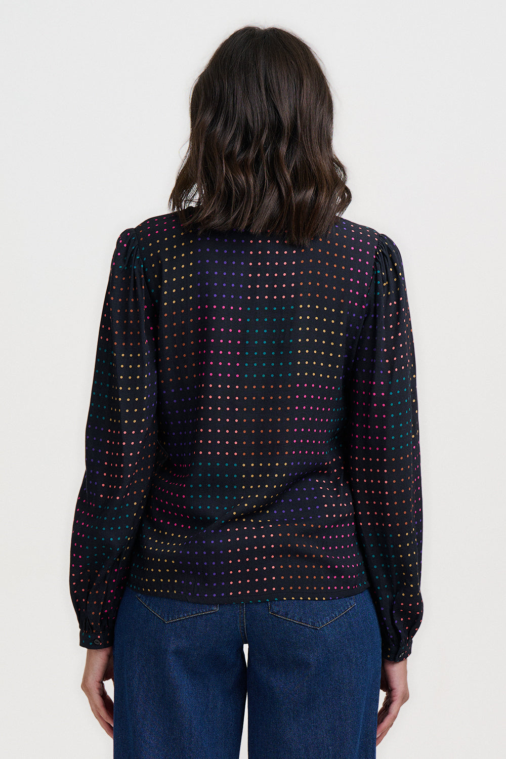 Person wearing a patterned black shirt with colorful dots and blue jeans on a white background