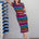 Woman wearing a colorful striped dress standing next to a rack of shoes against a plain wall.