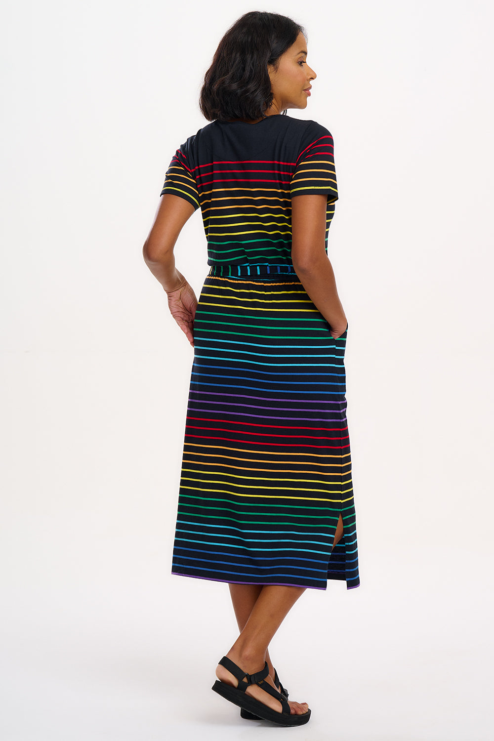 A model wearing a midi-length jersey dress with a black background featuring a vibrant multicolour striped pattern. The dress has a t-shirt fit with a matching tie belt and short sleeves.
