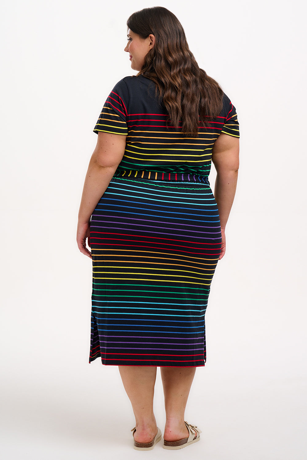 A model wearing a midi-length jersey dress with a black background featuring a vibrant multicolour striped pattern. The dress has a t-shirt fit with a matching tie belt and short sleeves.