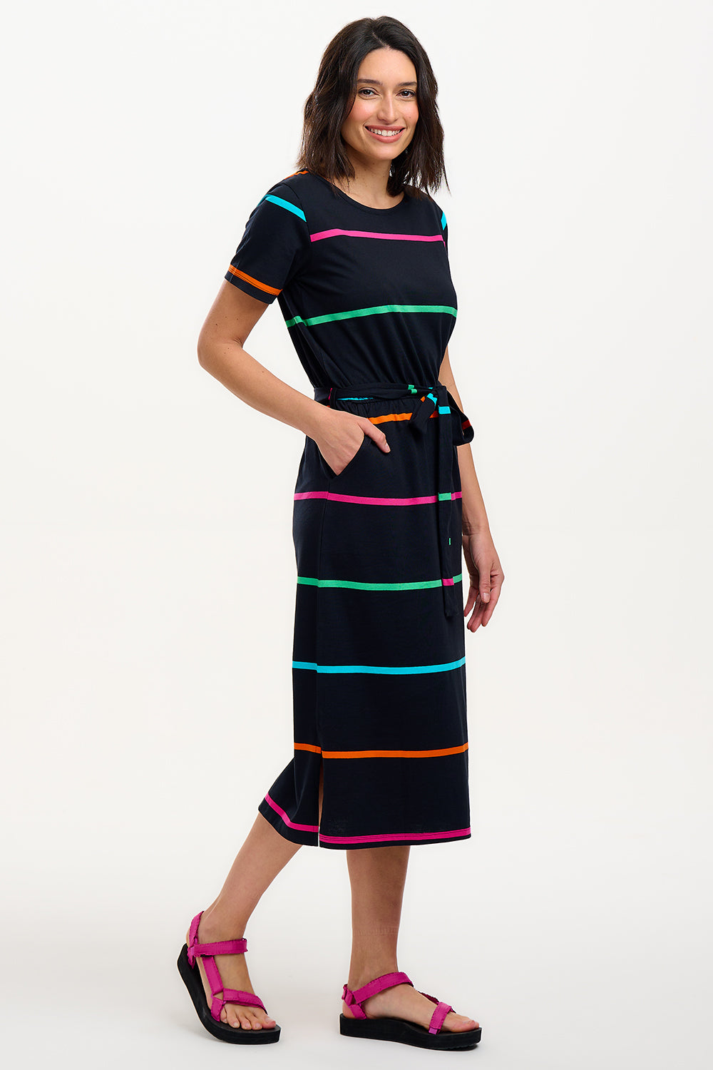 A model wearing a midi-length black dress with vibrant colored stripes, featuring a matching tie belt and short sleeves.