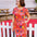 Woman wearing a colorful floral dress standing in front of a white picket fence.