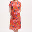 A model wearing a red jersey midi dress with a colorful tropical leaf and flower print, standing against a plain background.