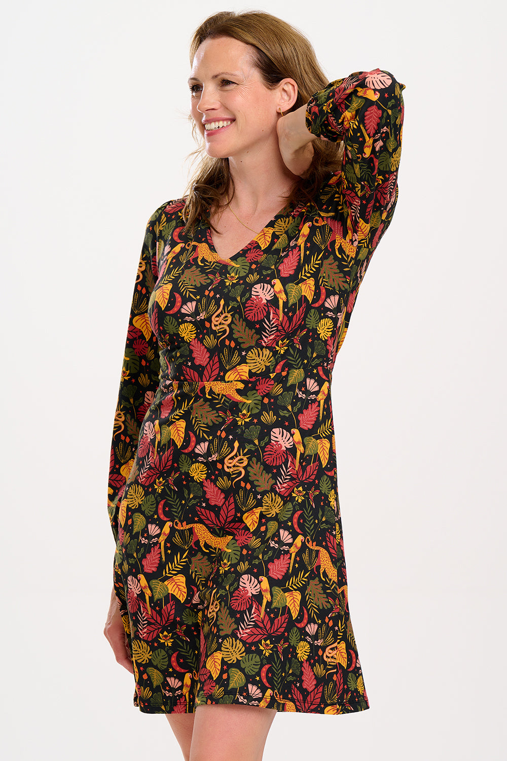 A woman smiling and posing in a black, earth toned mini jersey dress with long sleeves and a gathered design.