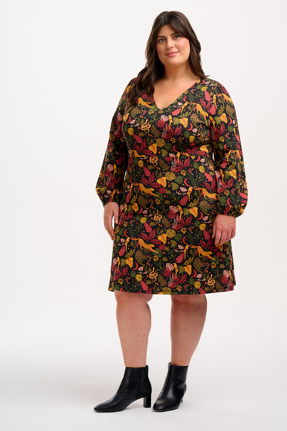 A woman smiling and posing in a black, earth toned mini jersey dress with long sleeves and a gathered design.