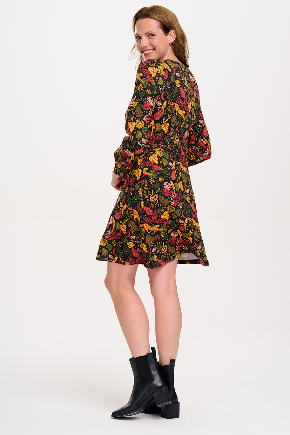 A woman smiling and posing in a black, earth toned mini jersey dress with long sleeves and a gathered design.