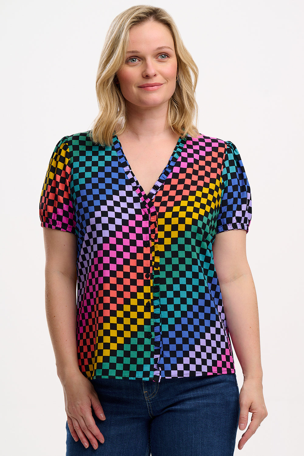 A woman wearing a short-sleeved, multicolored checkered blouse with frill trim and elasticated cuffs, paired with jeans.