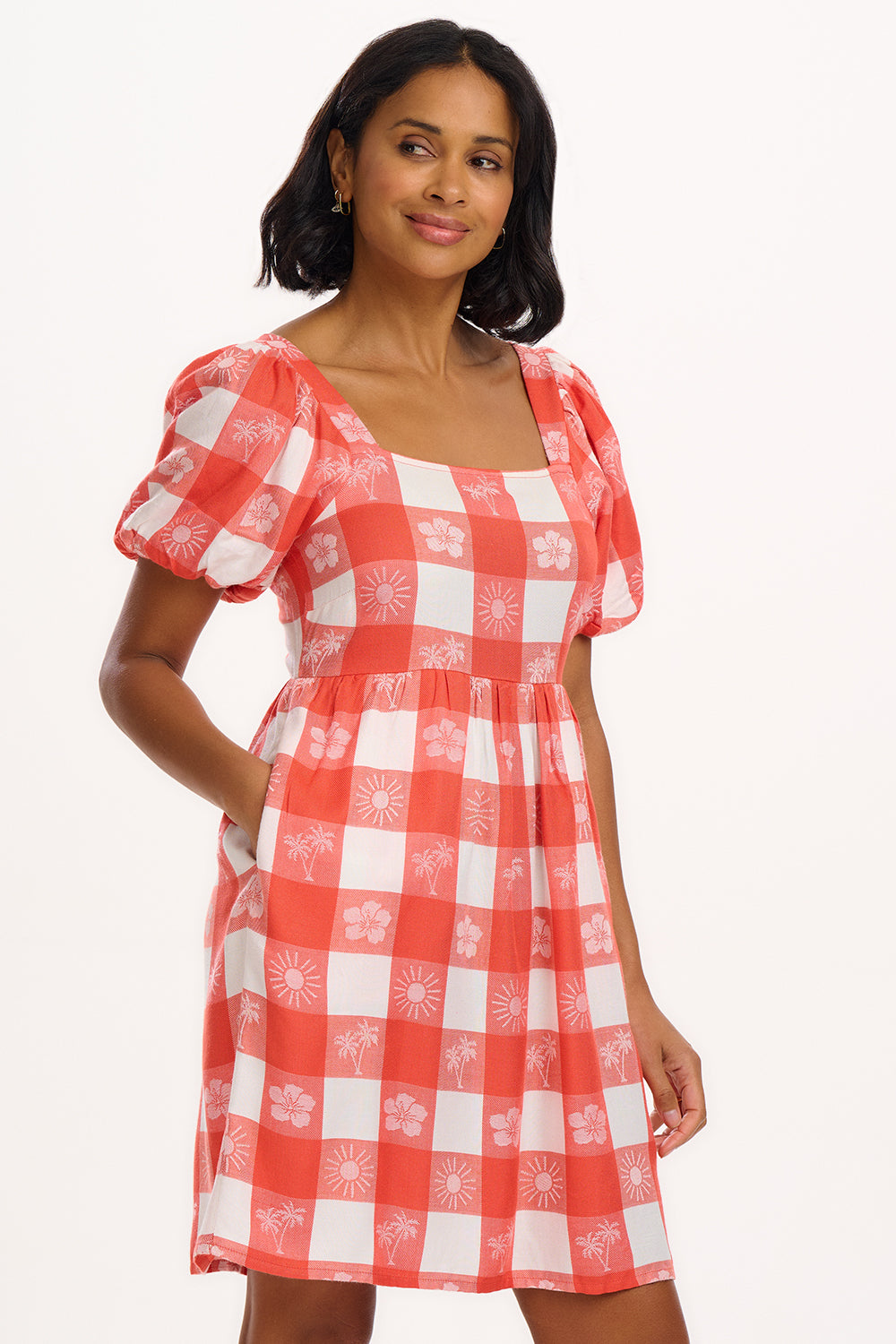 A woman wearing an off-white and coral gingham mini dress with puff sleeves and a tailored waist.