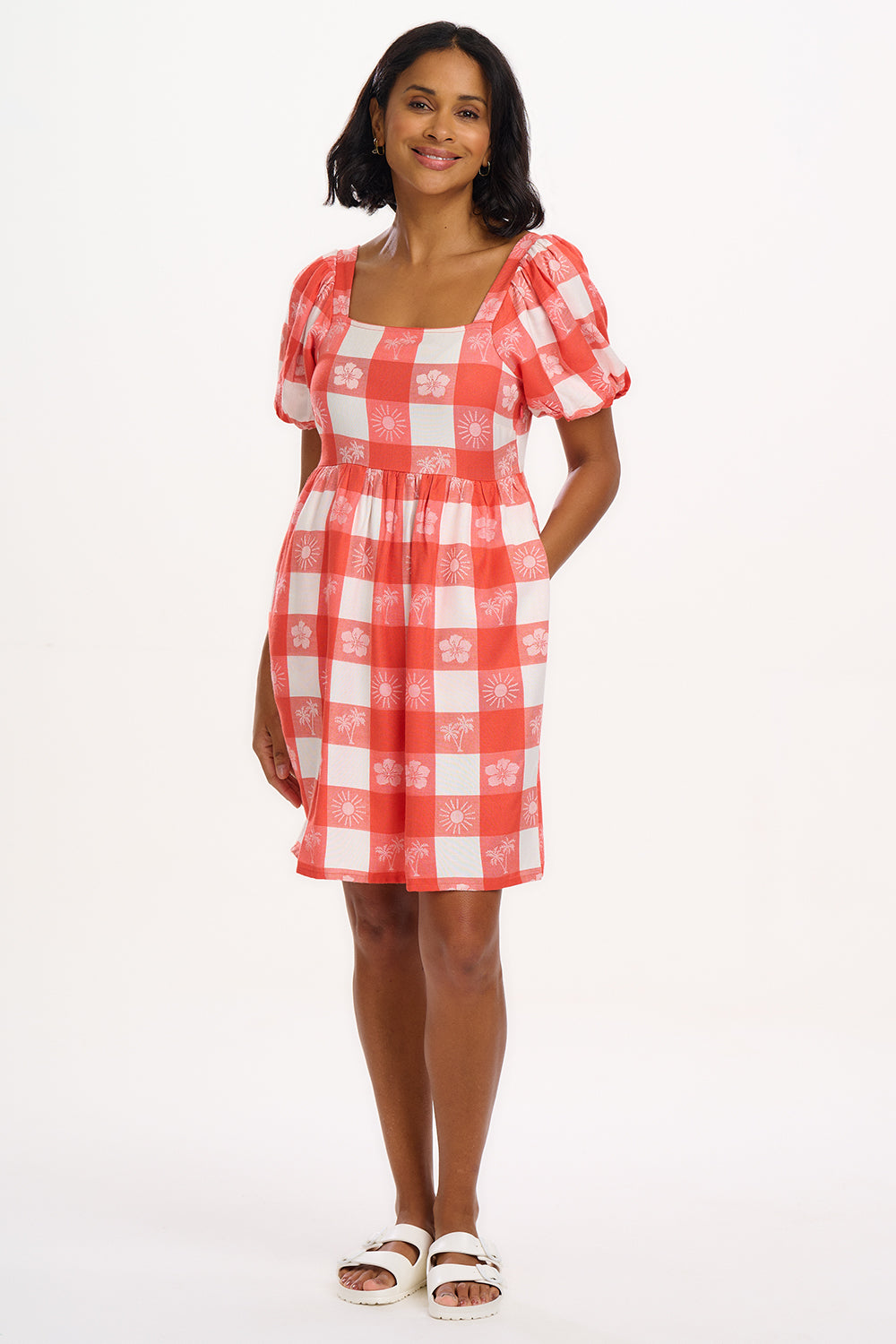 A woman wearing an off-white and coral gingham mini dress with puff sleeves and a tailored waist.