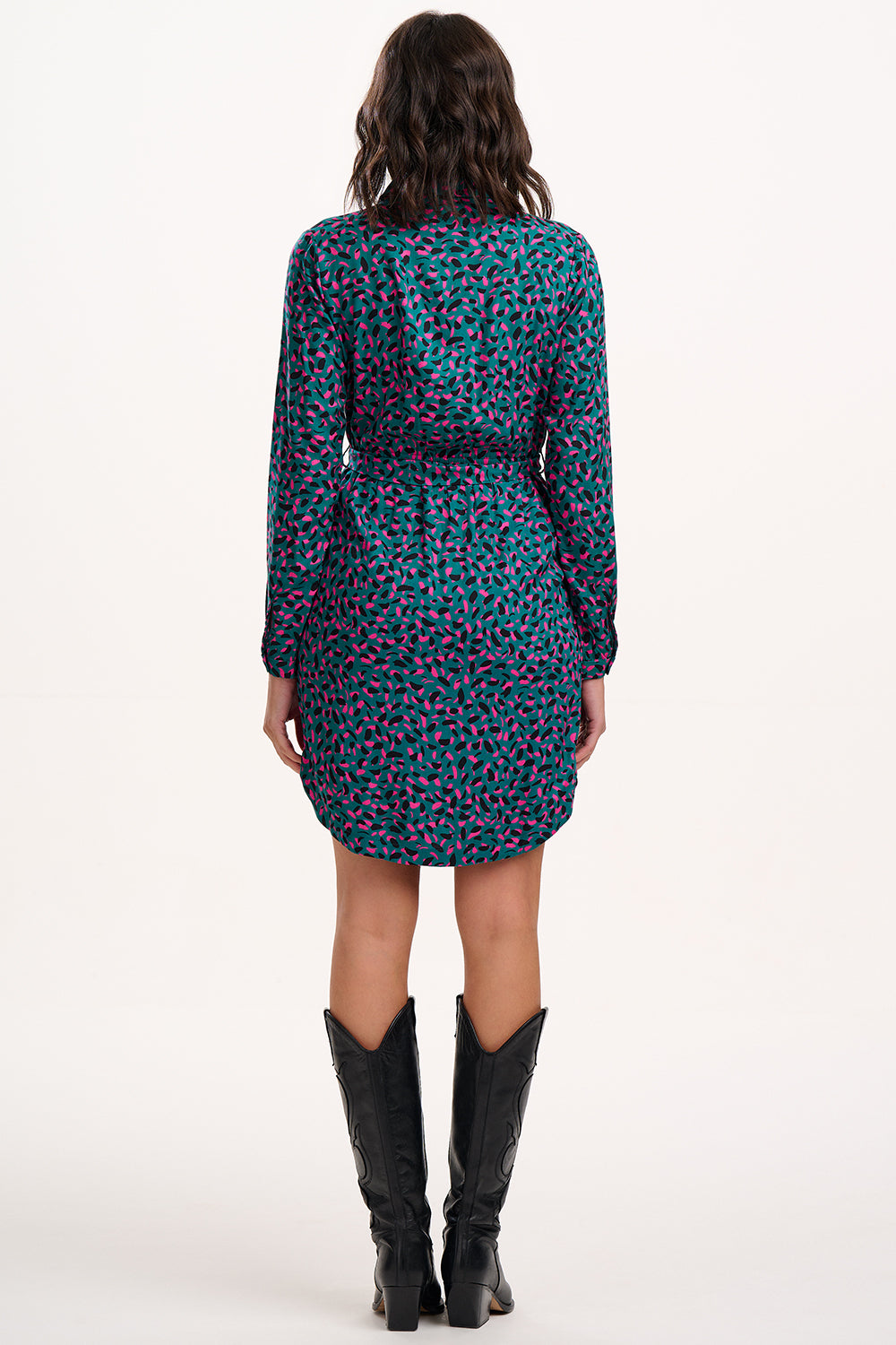 Woman wearing a patterned dress with long sleeves and black knee-high boots on a white background