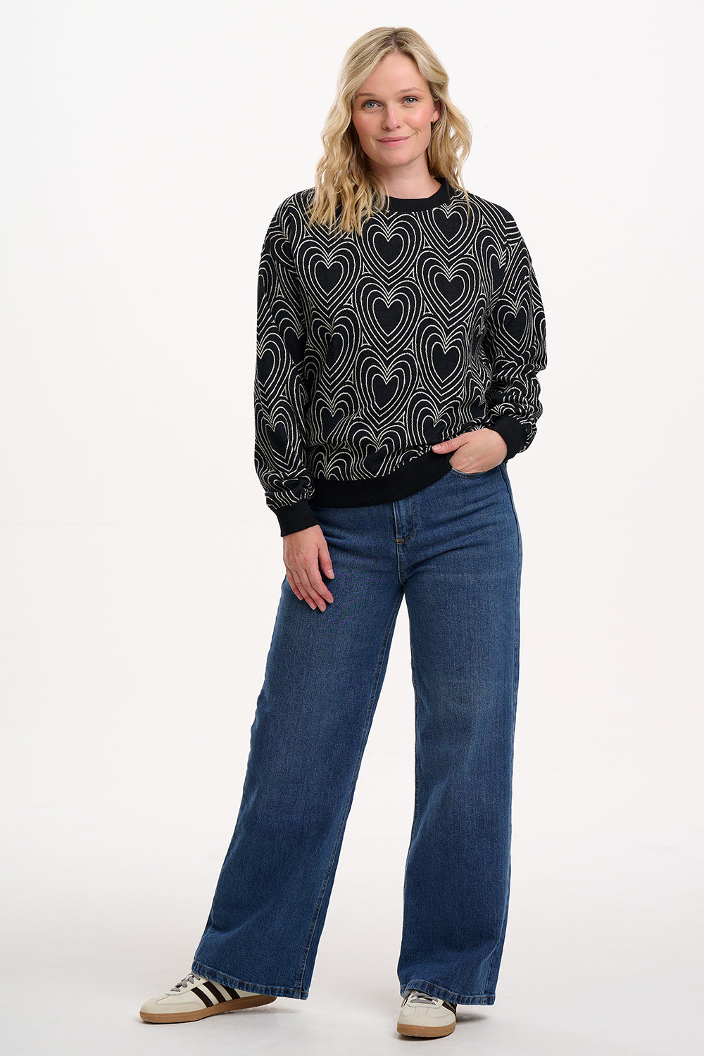 Woman wearing a black patterned sweater and blue jeans on a white background