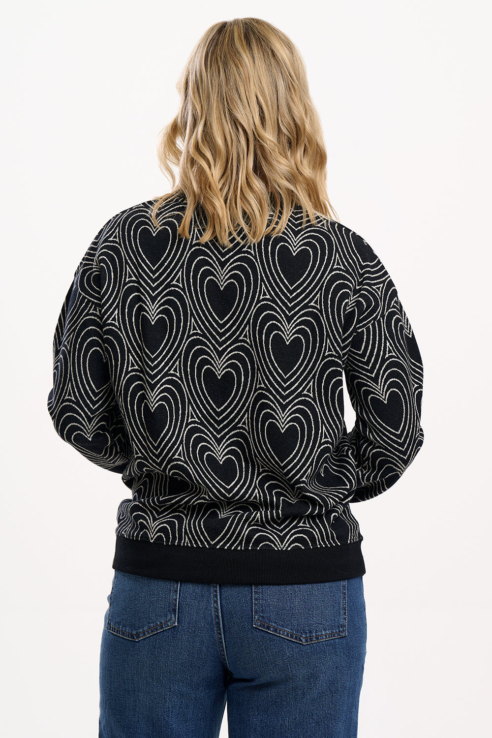Person wearing a black bomber jacket with heart pattern on the back, standing against a white background.