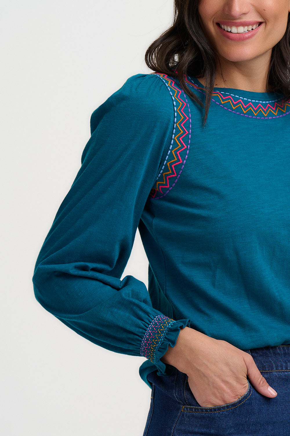 Woman wearing a teal blouse with colorful embroidery on a white background