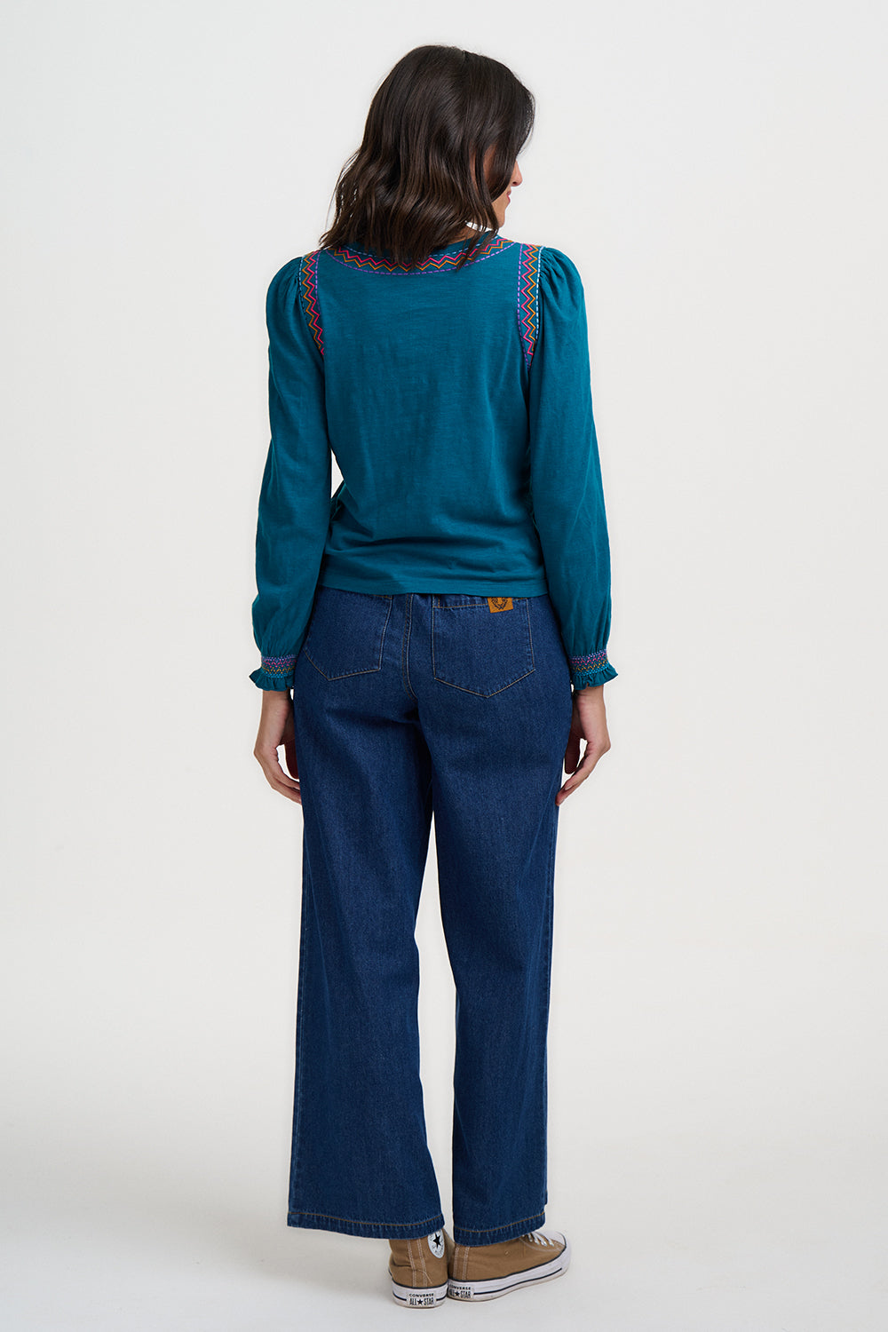 Person wearing a teal sweater and blue jeans on a white background