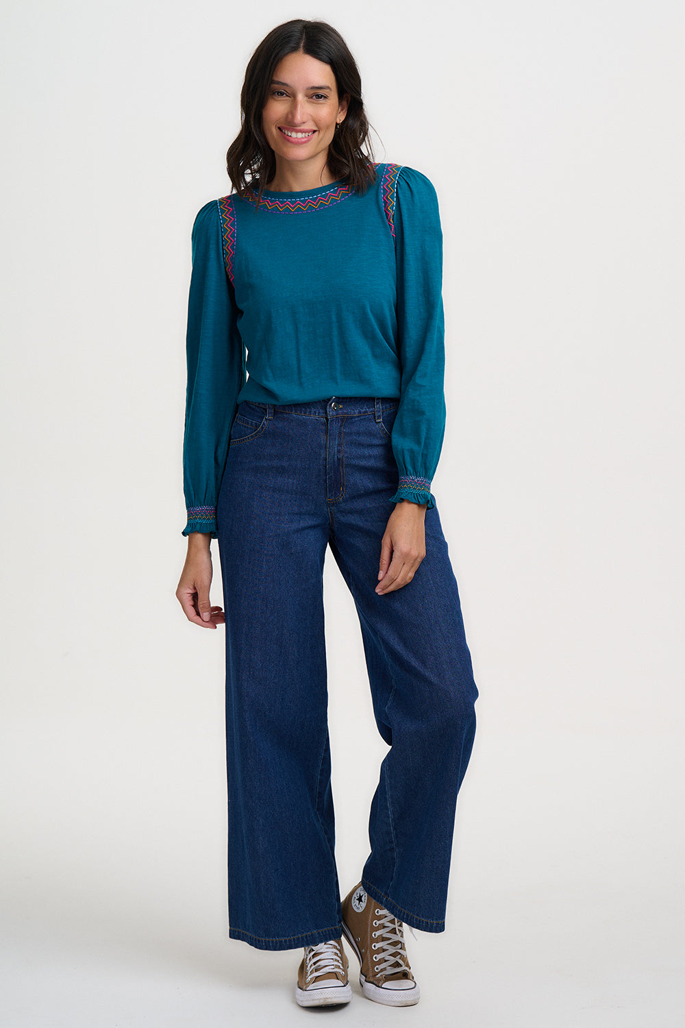 Woman wearing a teal blouse and blue jeans on a white background
