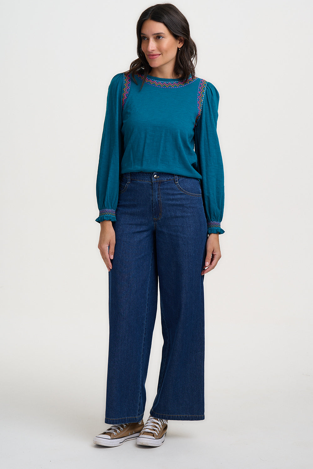 Woman wearing a teal sweater and blue jeans on a white background