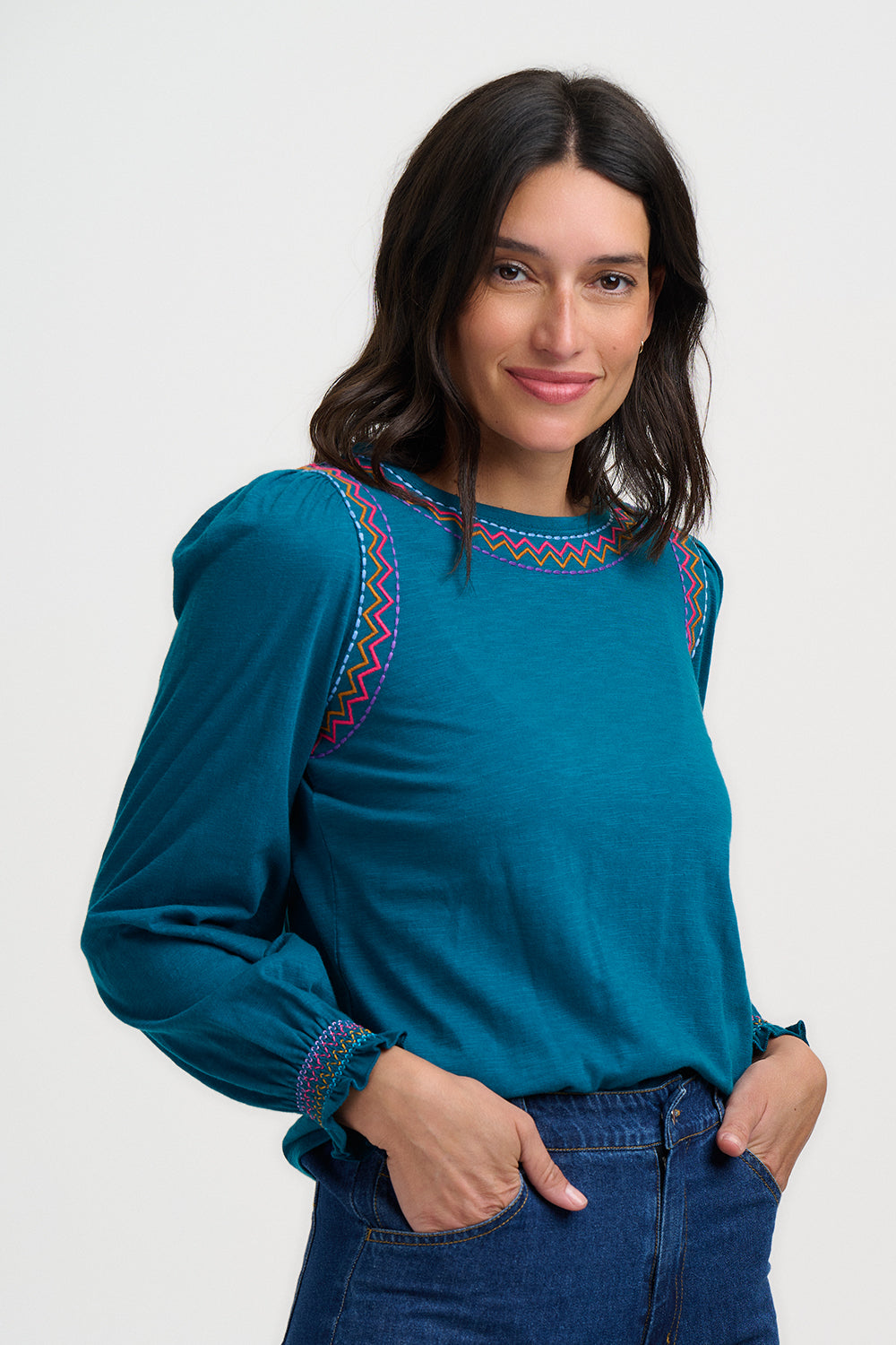 Woman wearing a teal blouse with colorful embroidery on a white background