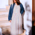 Woman in a striped dress and denim jacket standing on stone steps.