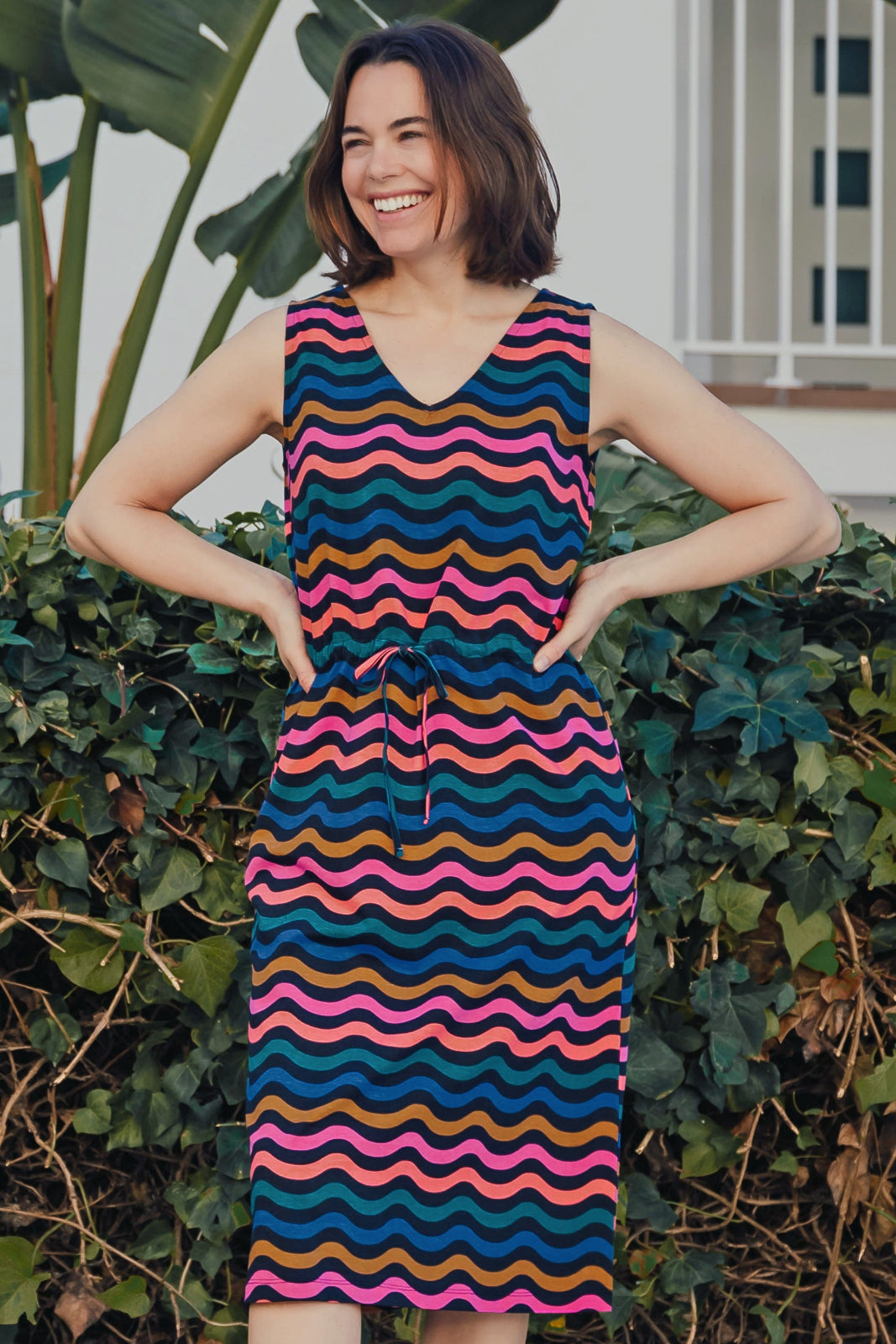 A model wearing a sleeveless, v-neck, midi dress with a wavy chevron stripe pattern in black, blue, pink, and orange.