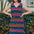 A model wearing a sleeveless, v-neck, midi dress with a wavy chevron stripe pattern in black, blue, pink, and orange.