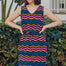 A model wearing a sleeveless, v-neck, midi dress with a wavy chevron stripe pattern in black, blue, pink, and orange.